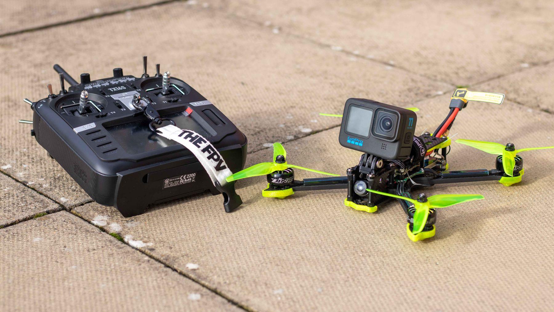 An FPV quadcopter with an action camera mounted on top, beside its radio controller