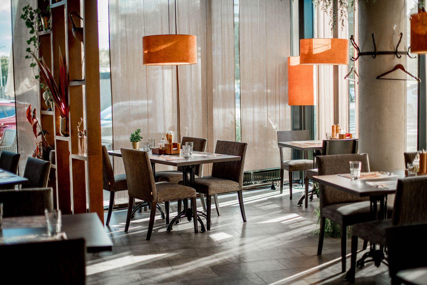 Restaurant dining room with set tables and pendant lamps beside a window